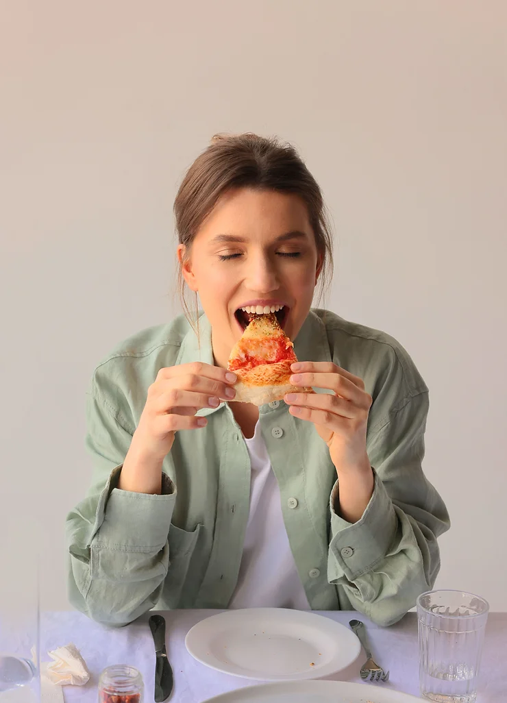 mulher comendo um pedaço de pizza com muita vontade.