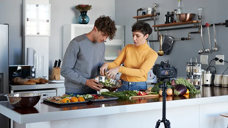 imagem de um homem e uma mulher gravando vídeos de receitas em um cozinha .