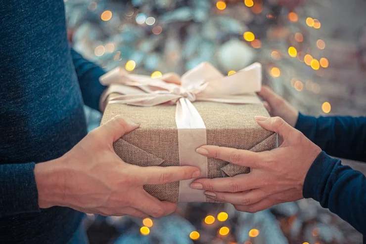 Uma pessoa entregando um presente simples, com as mãos envoltas em luz suave, representando afeto, empatia e conexão energética