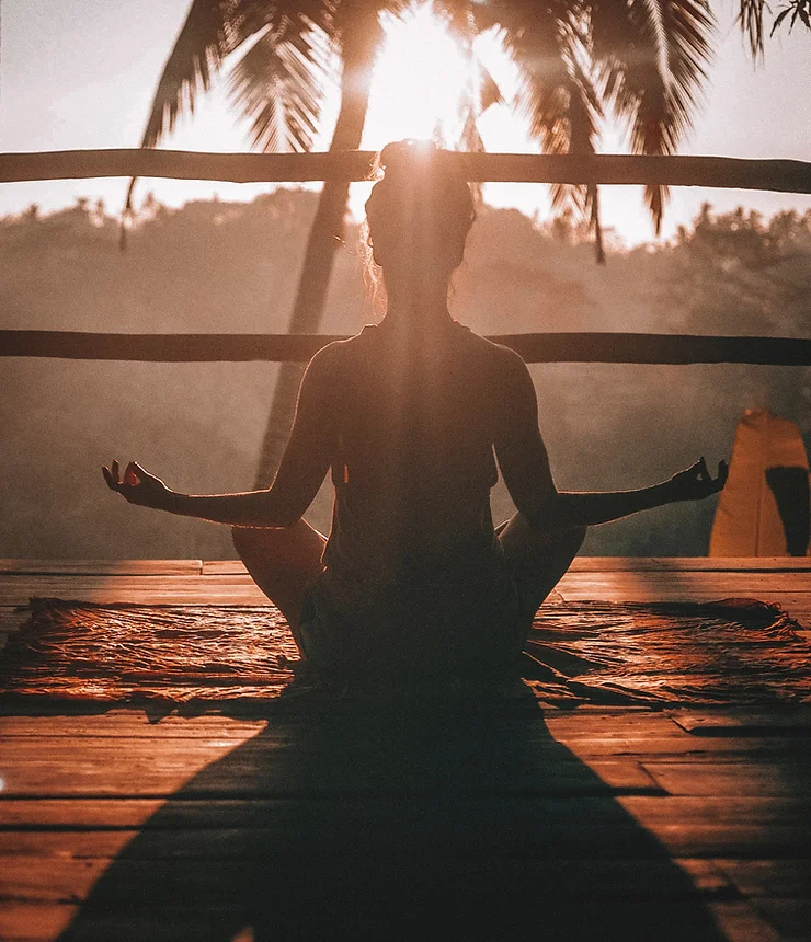 imagem de uma mulher meditando em um deck ao entardecer.
