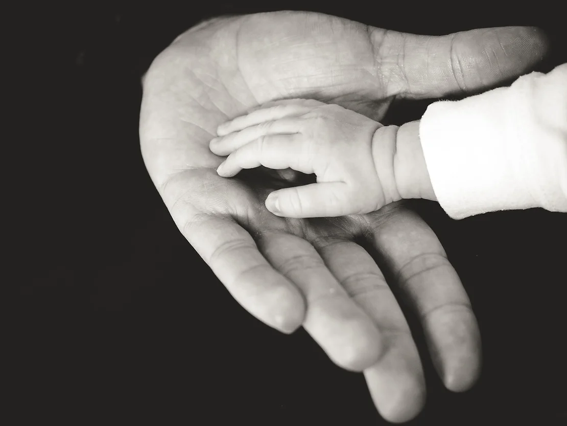 imagem da mão de um adulto segurando a mão de um bebe.
