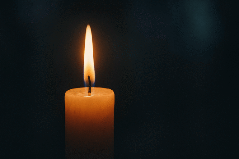 Vela acesa em um ambiente escuro, com chama dourada brilhando suavemente. O fundo está desfocado, criando uma atmosfera serena e introspectiva.